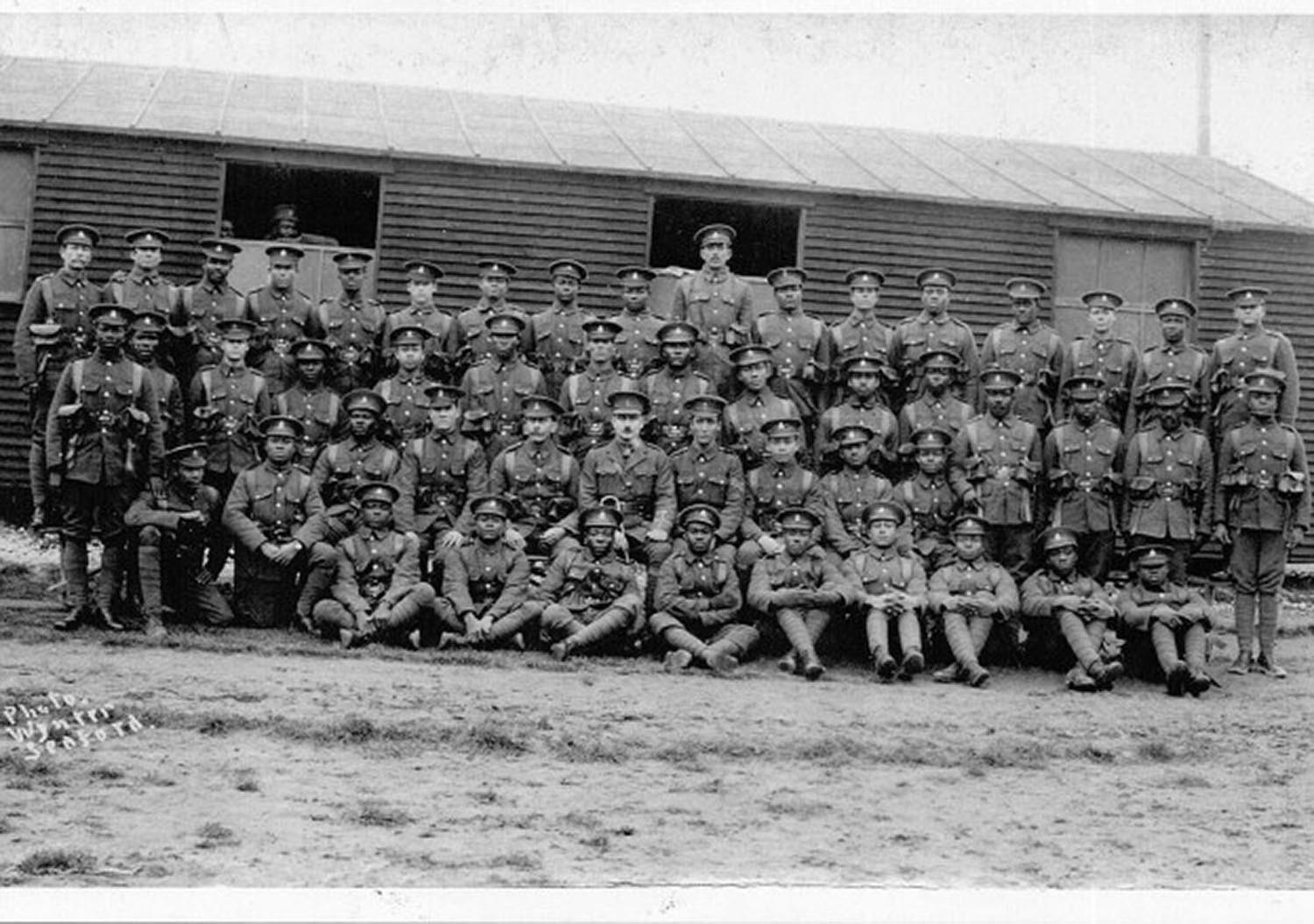 Black and white photograph showing four rows of troops arranged for the picture in front of their barracks