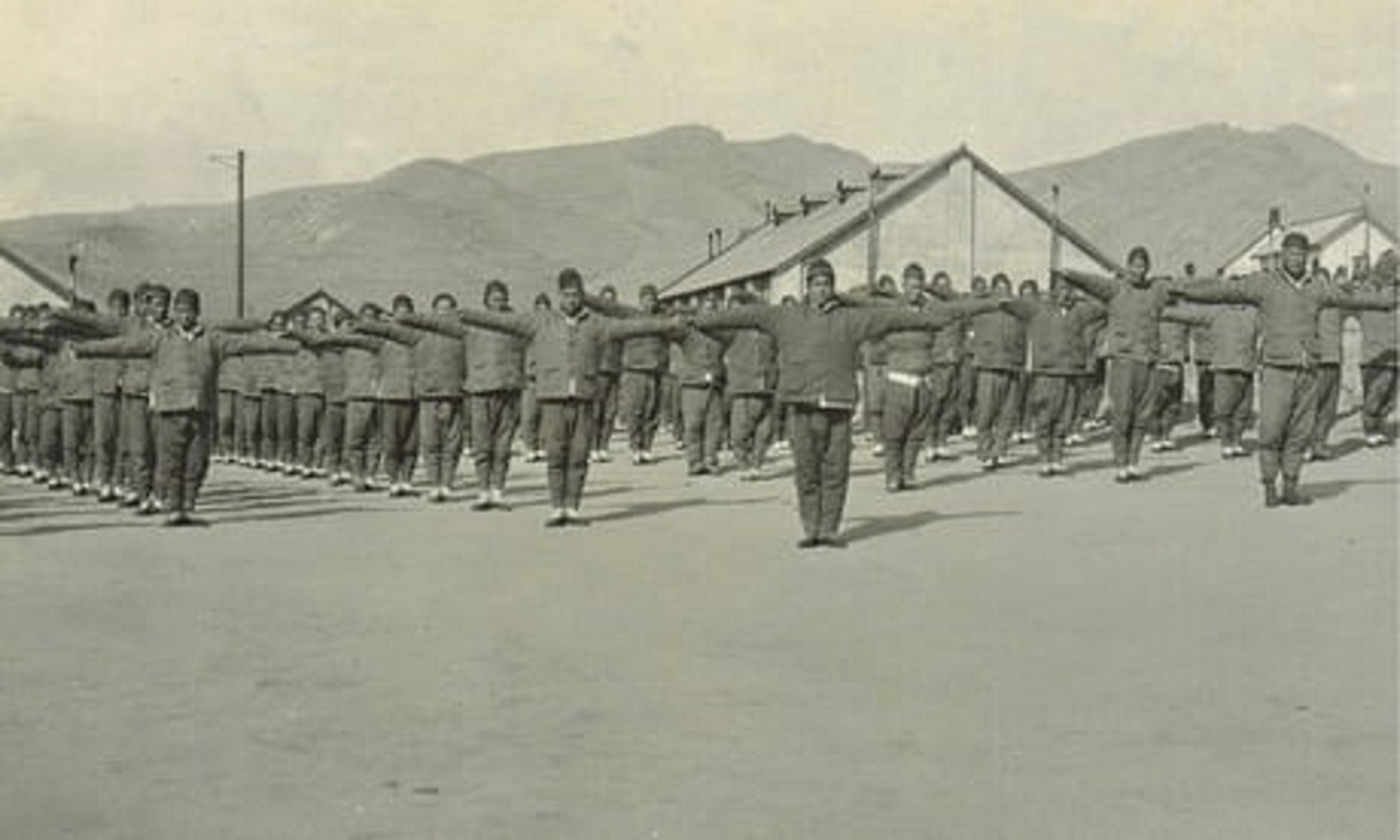 Black and white photograph showing Chineses workers excercising on a camp