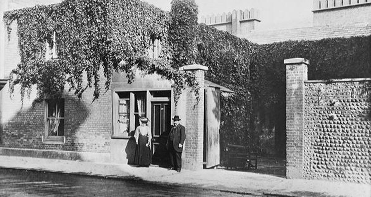 A photograph taken around 1900 of a couple standing outside an ivy-covered cottage
