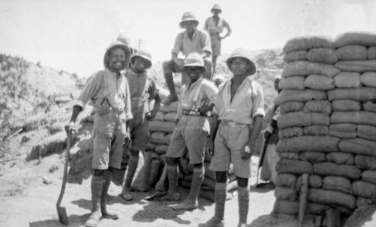 Black and white photograph showing troops of the BWIR standing by walls of protective sandbags