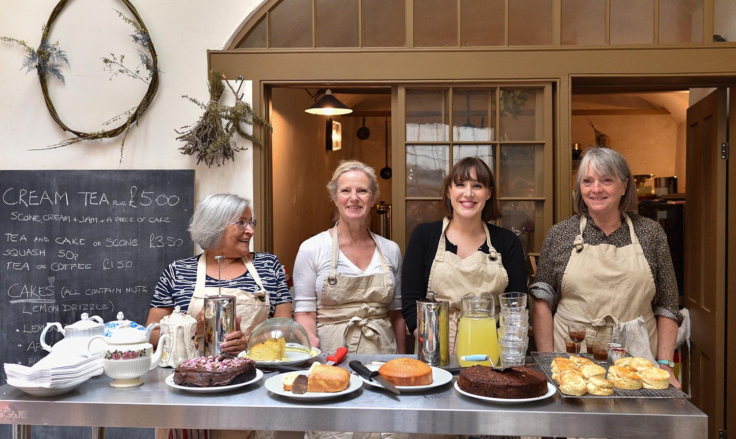Photograph showing four volunteers serving from behind a counter laden with cakes and refreshments