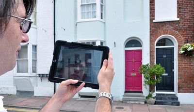 Photo looking over the shoulder of someone holding a tablet to view the house across the street